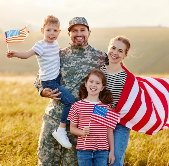 A heartwarming photo of a joyous family, holding American flags, proudly standing alongside a man dressed in an Army uniform, reflecting their shared patriotism, the honor of service, and the bond of family support.